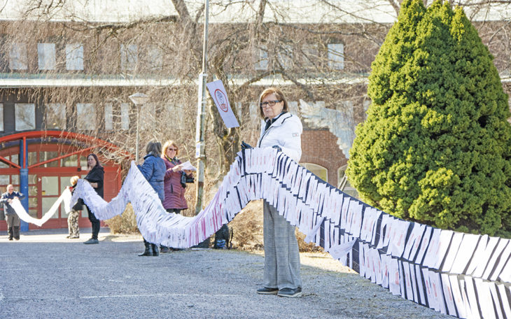 Bilden visar hur flera personer håller i den 60 meter långa gardinen. På gardinen är namnunderskrifterna fästade.