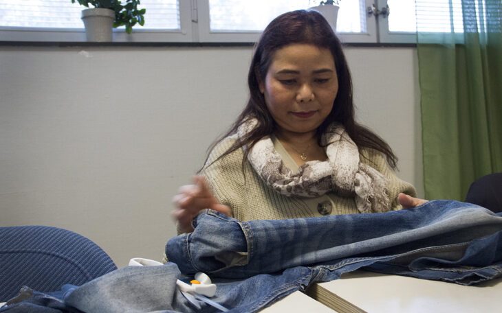 Thea Thanprasit, halvkroppasbild, sitter med jeans framför sig på bordet, på återbruksverkstaden.