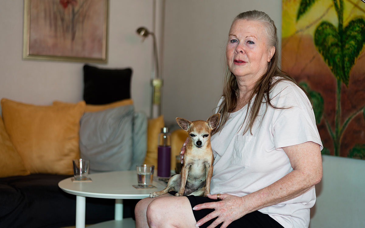 En kvinna som sitter i sitt vardagsrum med en liten hund i sitt knä.