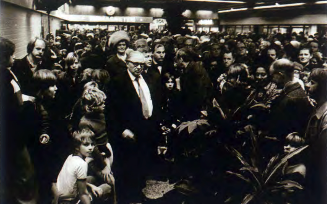 En svartvit bild där en man i kostym står i en folkmassa i ett köpcentrum.