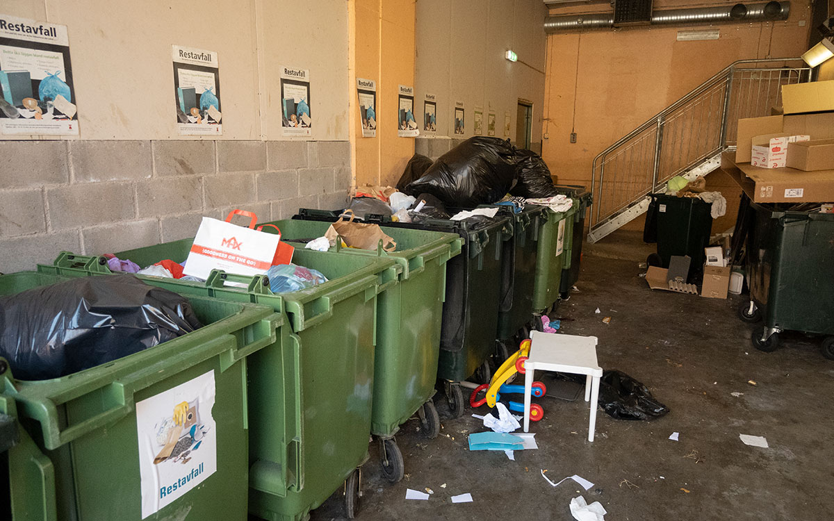 Ett överfullt soprum med diverse avfall både i överfulla soptunnor och på golvet.
