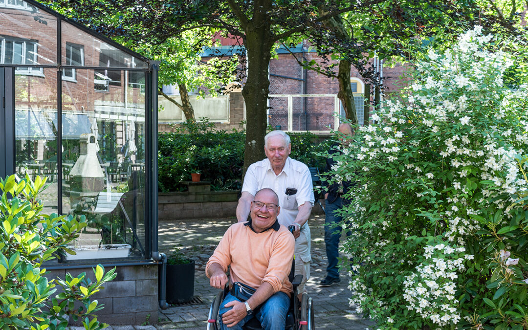 En äldre man står bakom en man som sitter i rullstol.