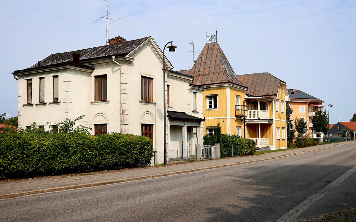 En gata med två lite äldre hus i förgrunden - ett vitt stenhus och ett gult trähus. I bakgrunden skymtar ett modernare flerfamiljshus. 