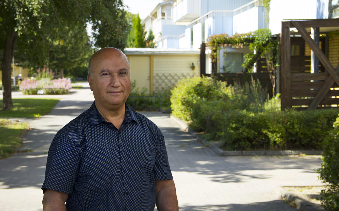 Halvkroppsporträtt på Gabriel Gabrö Agirman Beth-Qathe, som står i mörkblå kortärmad skjorta utomhus på en innergård där solen skiner och trädens skuggor syns på marken. I bakgrunden en gångväg, uteplatser, en husfasad, träd och grönska. Gabriel, som är hyresgäst, tycker att fler hyresvärdar borde ta tillvara möjligheten att installera solceller. Bland de värdar som har solceller är det än så länge ganska ovanligt att solelen går till hyresgästernas hushållsel.