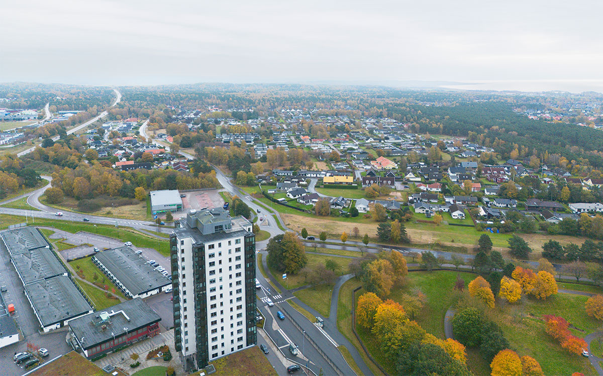 En bild tagen från luften som i förgrunden visar ett vitt sextonvåningshus och i bakgrunden bebyggelse, landsvägar, höstgula träd och havet.