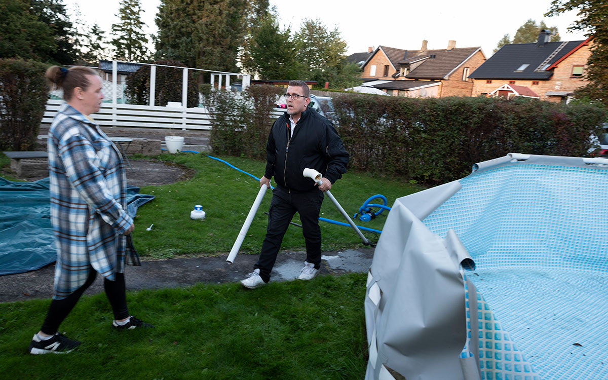 En man som håller i rör som tillhör en delvis demonterad pool och en kvinna som går mot poolen.