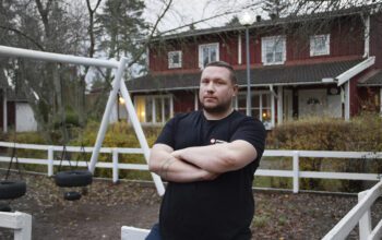 Jacop Lindholm, halvkroppsporträtt, står med korslagda armar i en mörk tshirt framför en vitmålad gungställning inhängad med ett vitmålat staket. Han och grannarna har reagerat över att brister åtgärdats på ett slarvigt sätt.