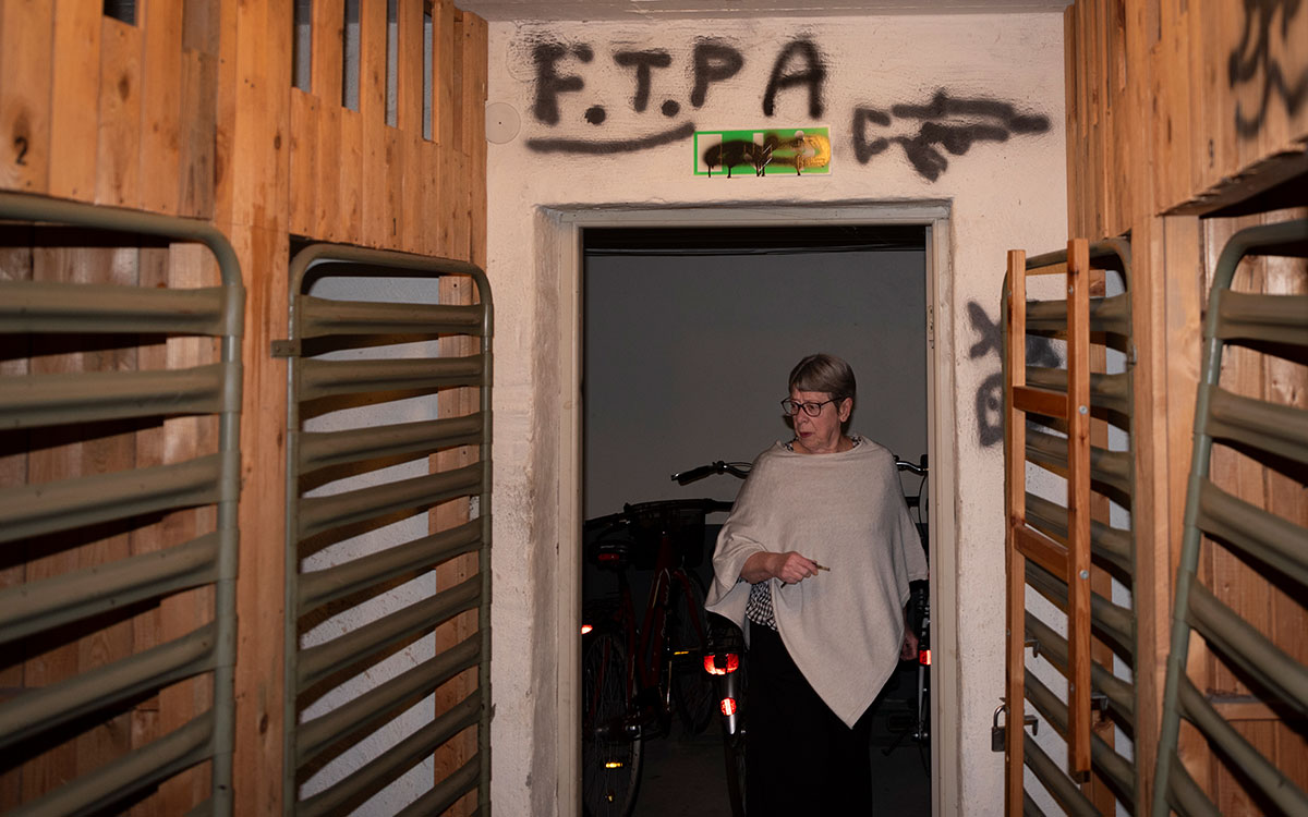 En äldre dam som tittar in i ett källarförråd där någon sprejmålat ett automatvapen samt texten "F.T.P" på väggen.