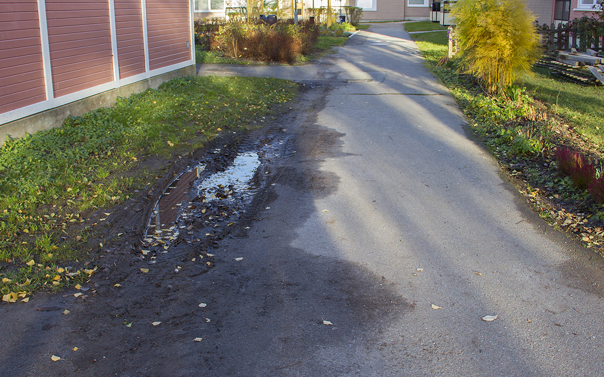 En gångväg. Till vänster leriga hjulspår i gräsmattan, till höger en rabatt. Rikshem har tagit bort staketet runt uteplatserna för två hyresgäster i Gränby i samband med att ytor för brandstegar anlades.