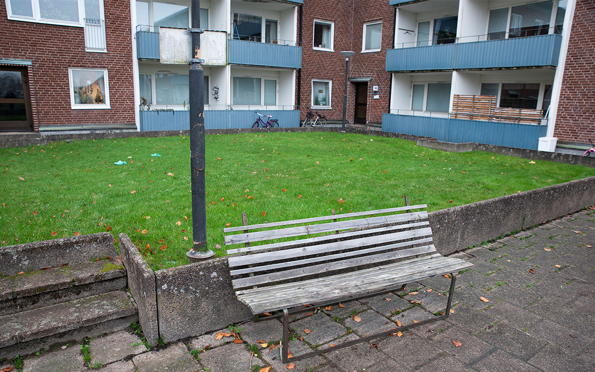 En sliten bänk framför en gräsmatta framför ett tegelhus med balkonger.