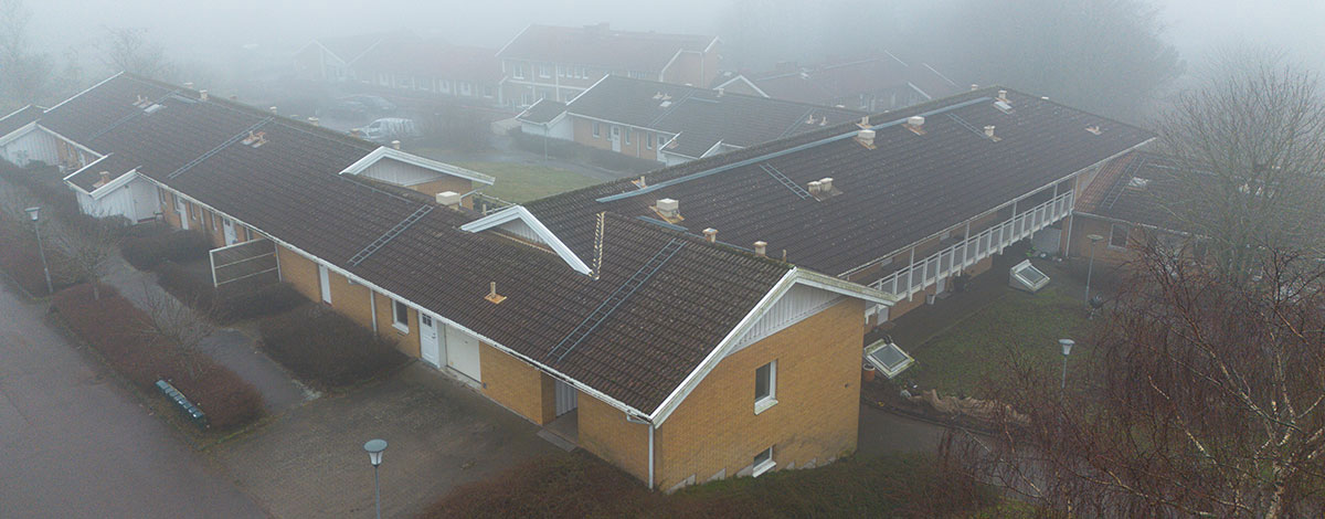 En bild tagen ovanifrån som visar flera ihopbyggda bostadshus i gult tegel en dimmig dag.