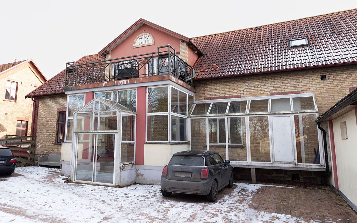 Ett tvåvåningshus i gult tegel, glasveranda och texten "hotel árbájt" och på gården framför snö.