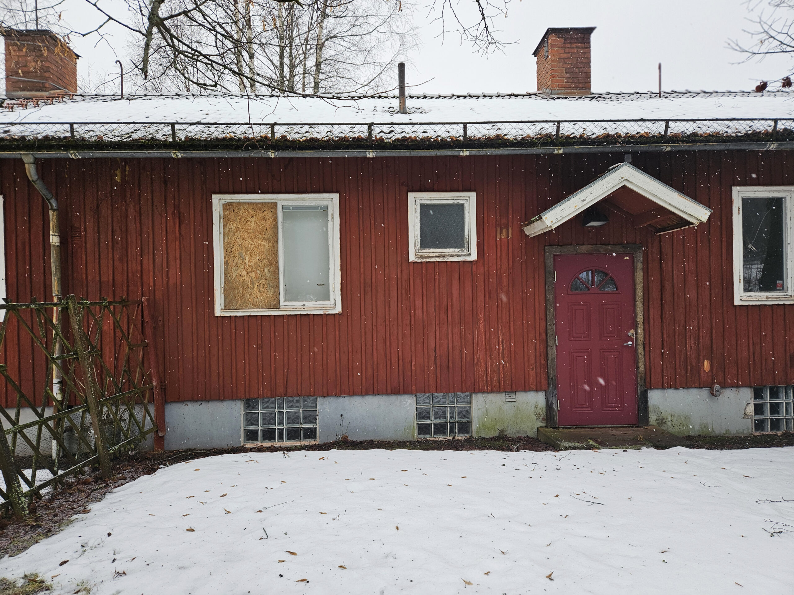 Ett rött hus med ett fönster som täcks av en träskiva.