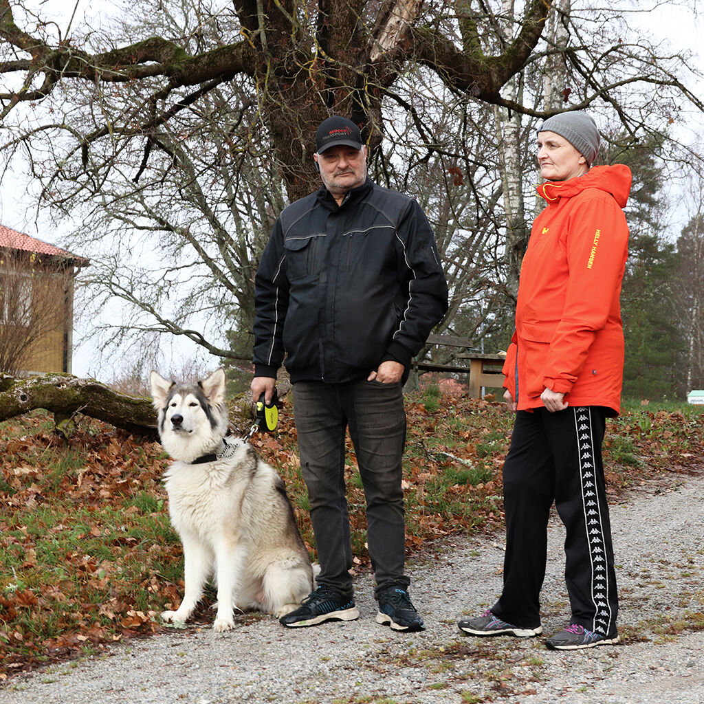 Bild på en man och en kvinna. Mannen håller en stor hund i koppel. I bakgrunden syns ett träd och en del av ett flerfamiljshus.