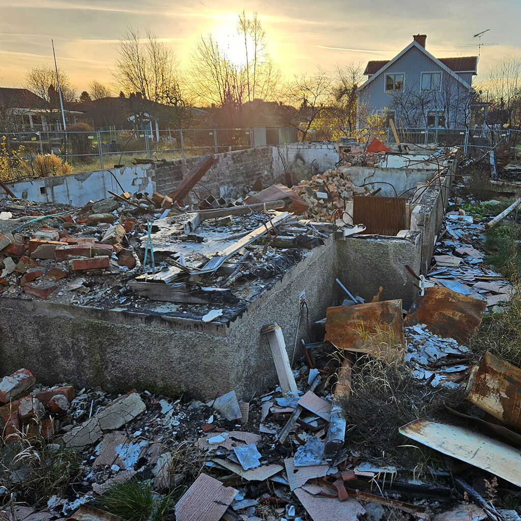 Rester av en husgrund och en massa bråte som ligger på en tomt.